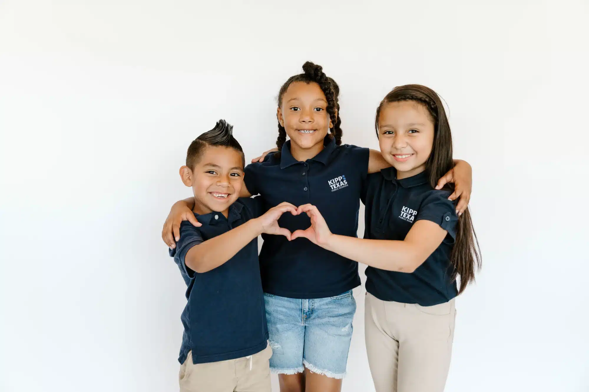 Three KIPP students smiling, making heart logo with hands